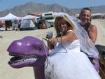 The happy couple rides off into the desert mirage on their purple dinosaur.